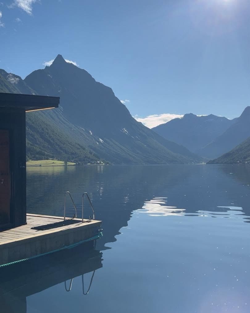 Hjørnet av badstua og badestigen mot blank fjord, med fjell som blir lysare mot horisonten.
